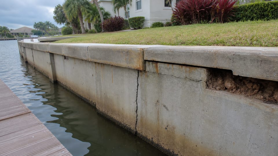 Illustration of a concrete seawall with cracking, cap movement, rust staining, and a small soil void.