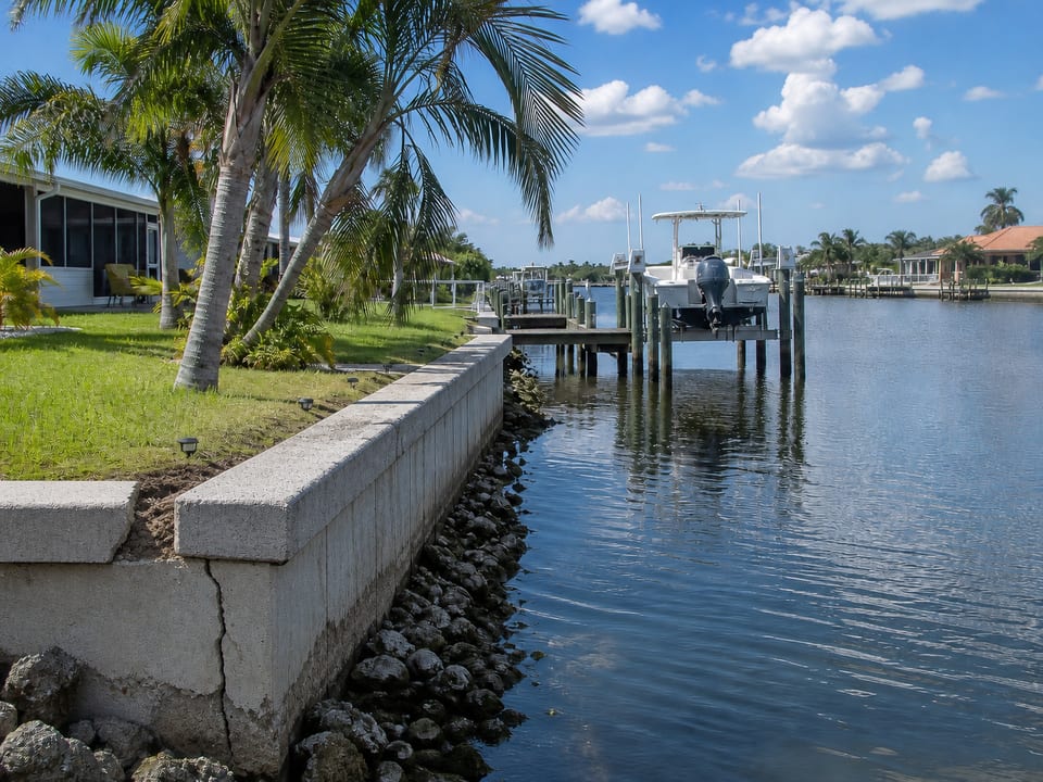 Illustration of a canal seawall with localized cracking and soil loss beside a waterfront home.