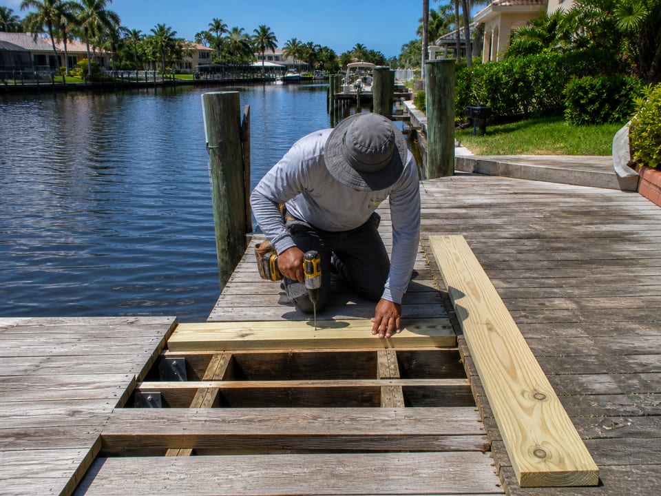 Illustration of a worker replacing a damaged board on an existing residential dock.