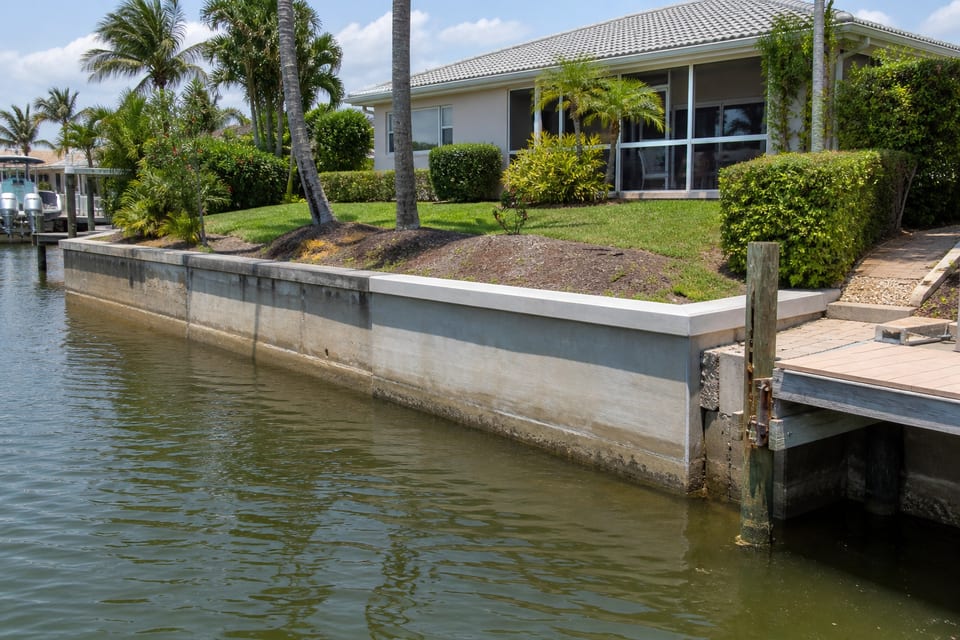 Illustration of a canal-front home with a concrete seawall, dock, and narrow shoreline access.